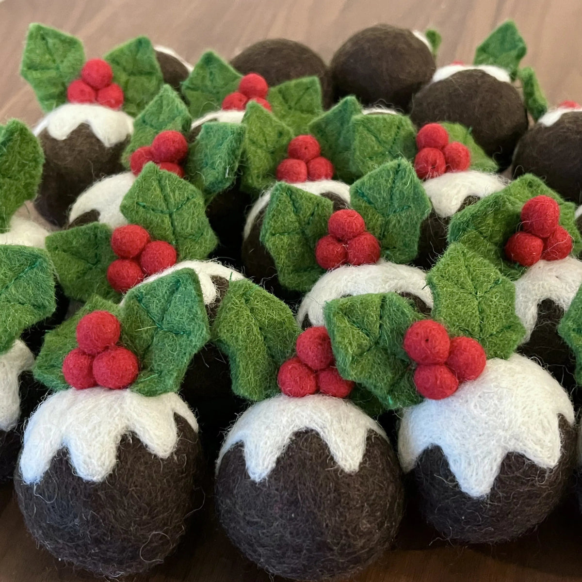 Handmade felted wool Christmas pudding cat toy balls with white icing, green holly leaves and red berries, grouped on a wooden table