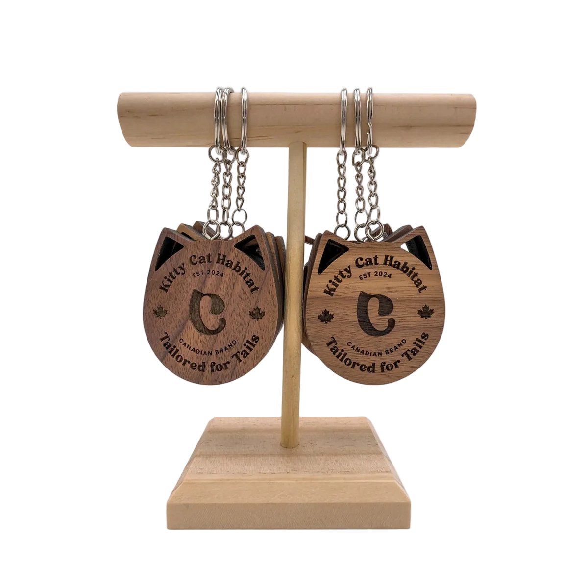 Several walnut wooden cat head keychains showing the logo side hanging on a wooden display stand on a light background.