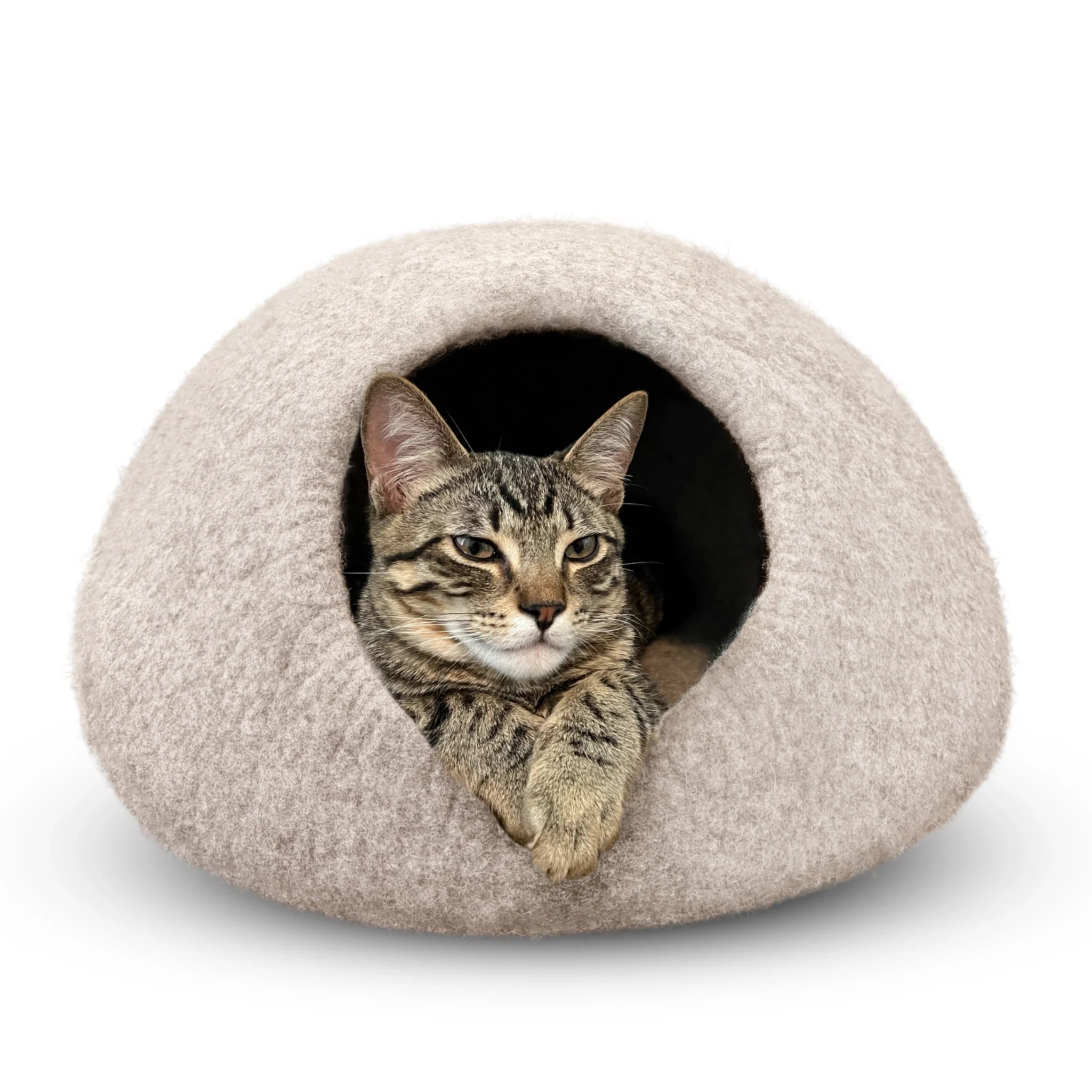 Tabby cat peeking out of a light brown felted wool cat cave bed on a white background