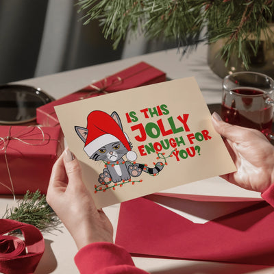 Hands holding the Christmas cat card at a table set with red wrapped gifts, a red envelope and a glass of mulled wine
