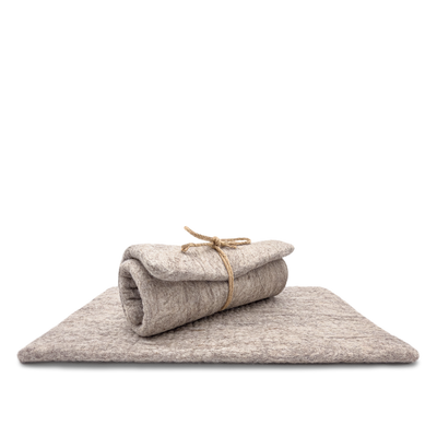 Light brown and grey rectangular felted wool cat carrier cushion rolled and tied with twine on a white background.