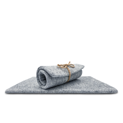 Light grey rectangular felted wool cat carrier cushion rolled and tied with twine on top of a flat pad.