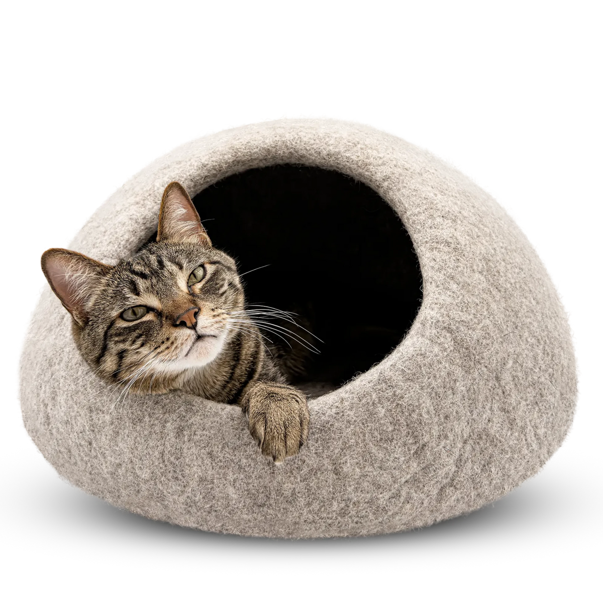 Tabby cat resting at the opening of a light brown felted wool cat cave bed on a white background