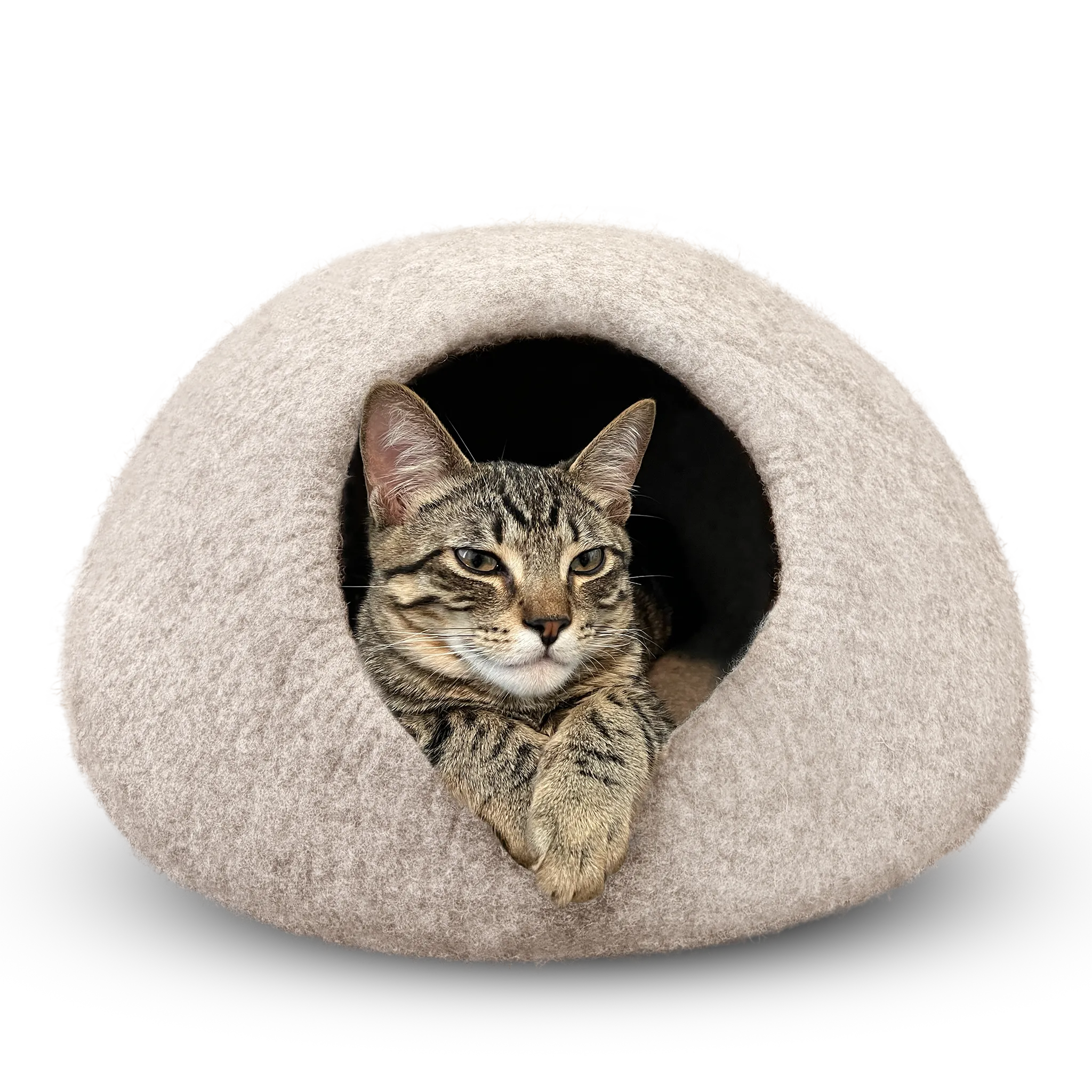 Tabby cat peeking out of a light brown felted wool cat cave bed on a white background