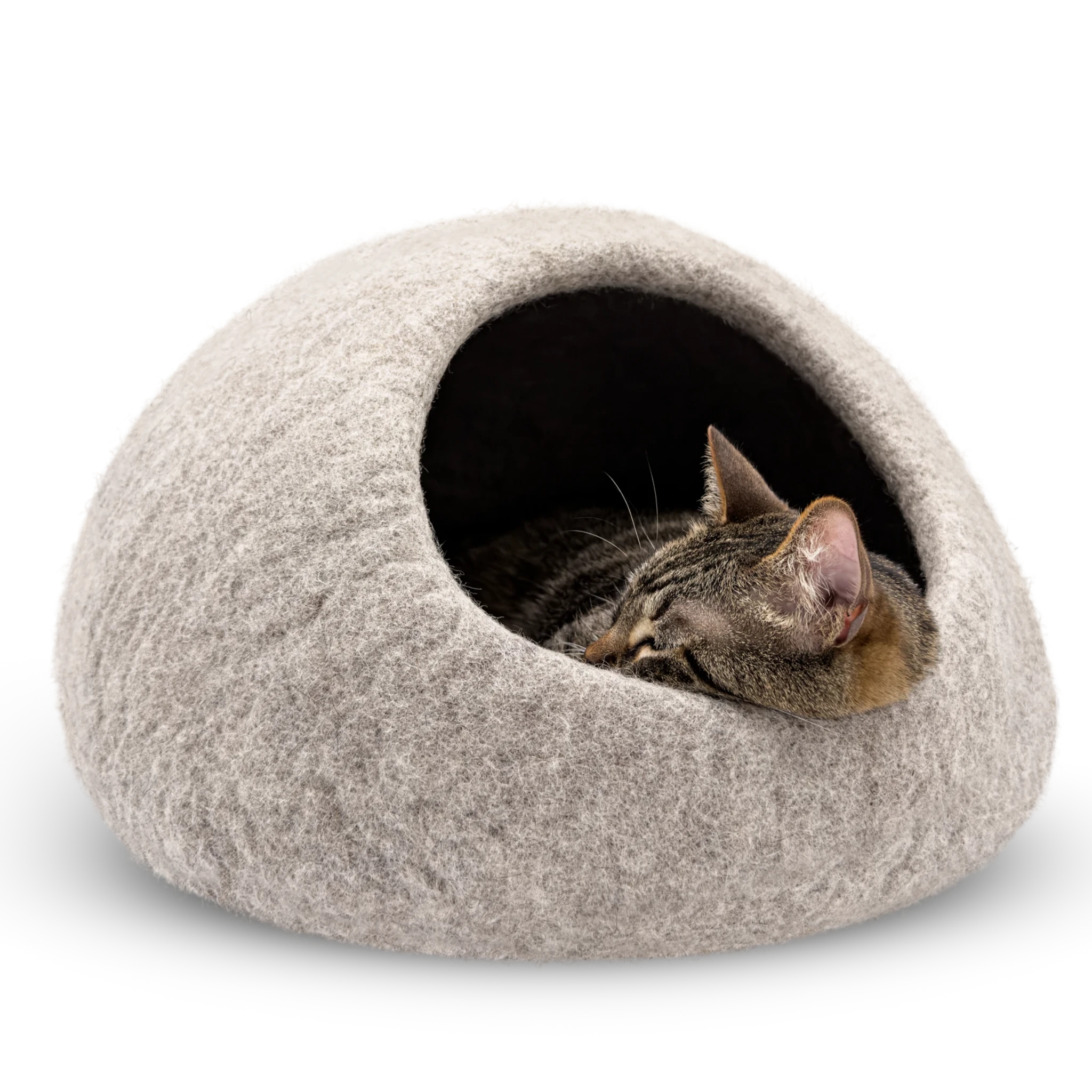 Tabby cat sleeping inside a light brown felted wool cat cave bed on a white background