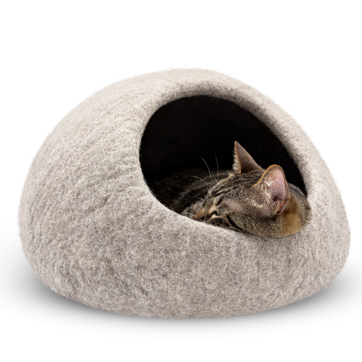 Tabby cat sleeping inside a light brown felted wool cat cave bed on a white background