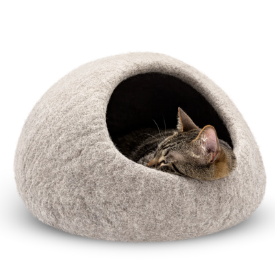 Tabby cat sleeping inside a light brown felted wool cat cave bed on a white background