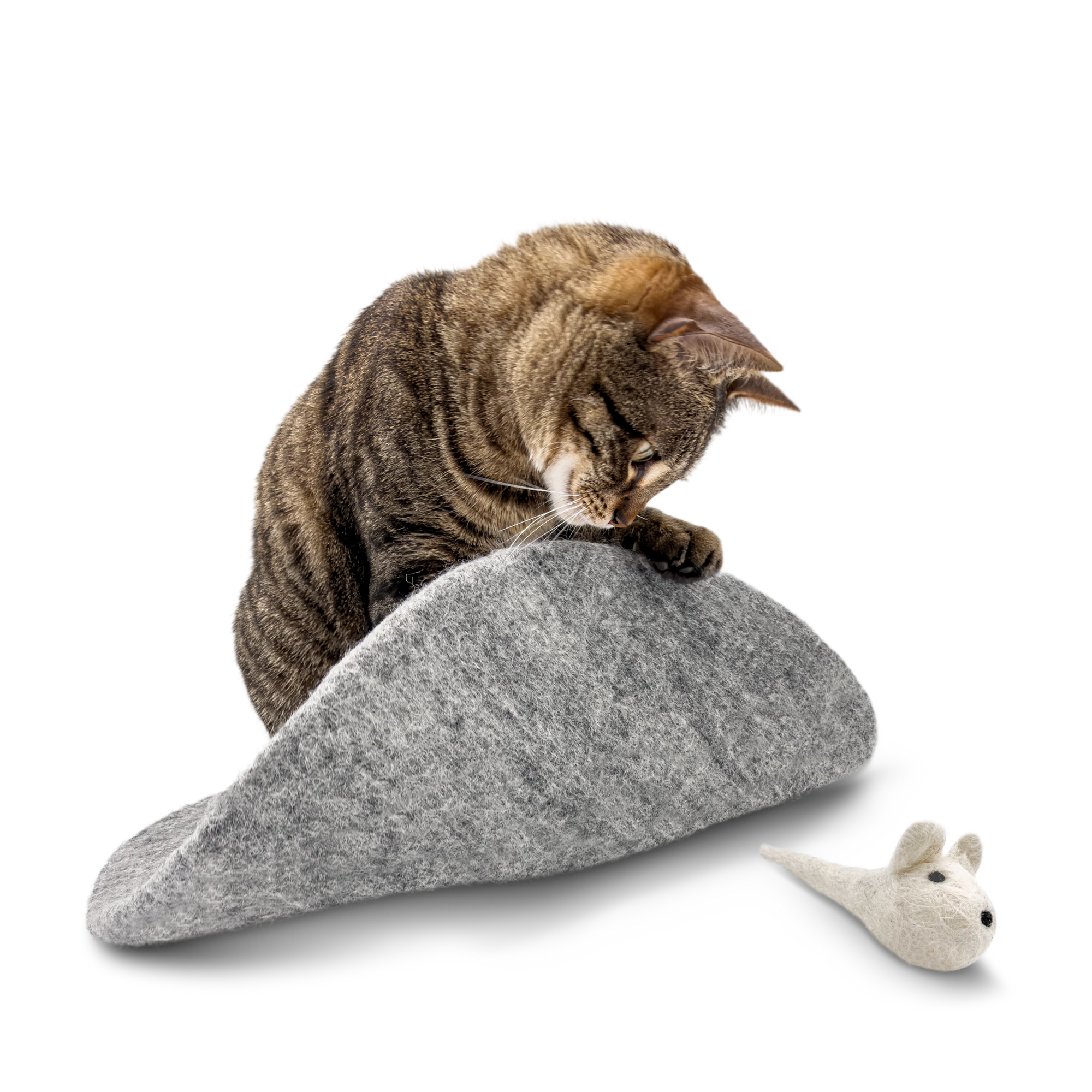 Tabby cat playing with a white felted wool mouse toy on a grey wool mat on a light background.