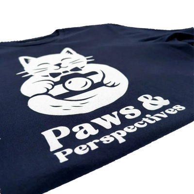 Close-upa angled photo of the white Paws & Perspectives cat graphic printed on a navy blue t-shirt on a light background.