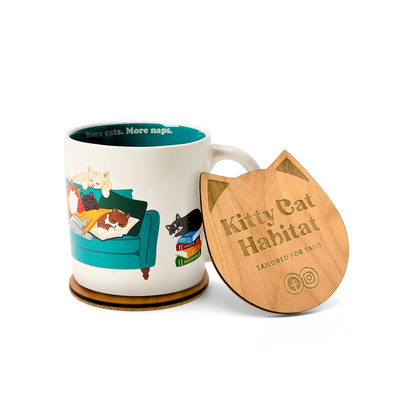 A ceramic mug with a colorful cat-themed illustration sits beside a wooden cat head shaped coaster. The lid is engraved with the text 'Kitty Cat Habitat' and 'TAILORED FOR TAILS'.
