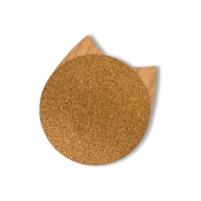 Wooden cat head drink coaster with cork backing facing forward and wood side peeking out behind on a light background.