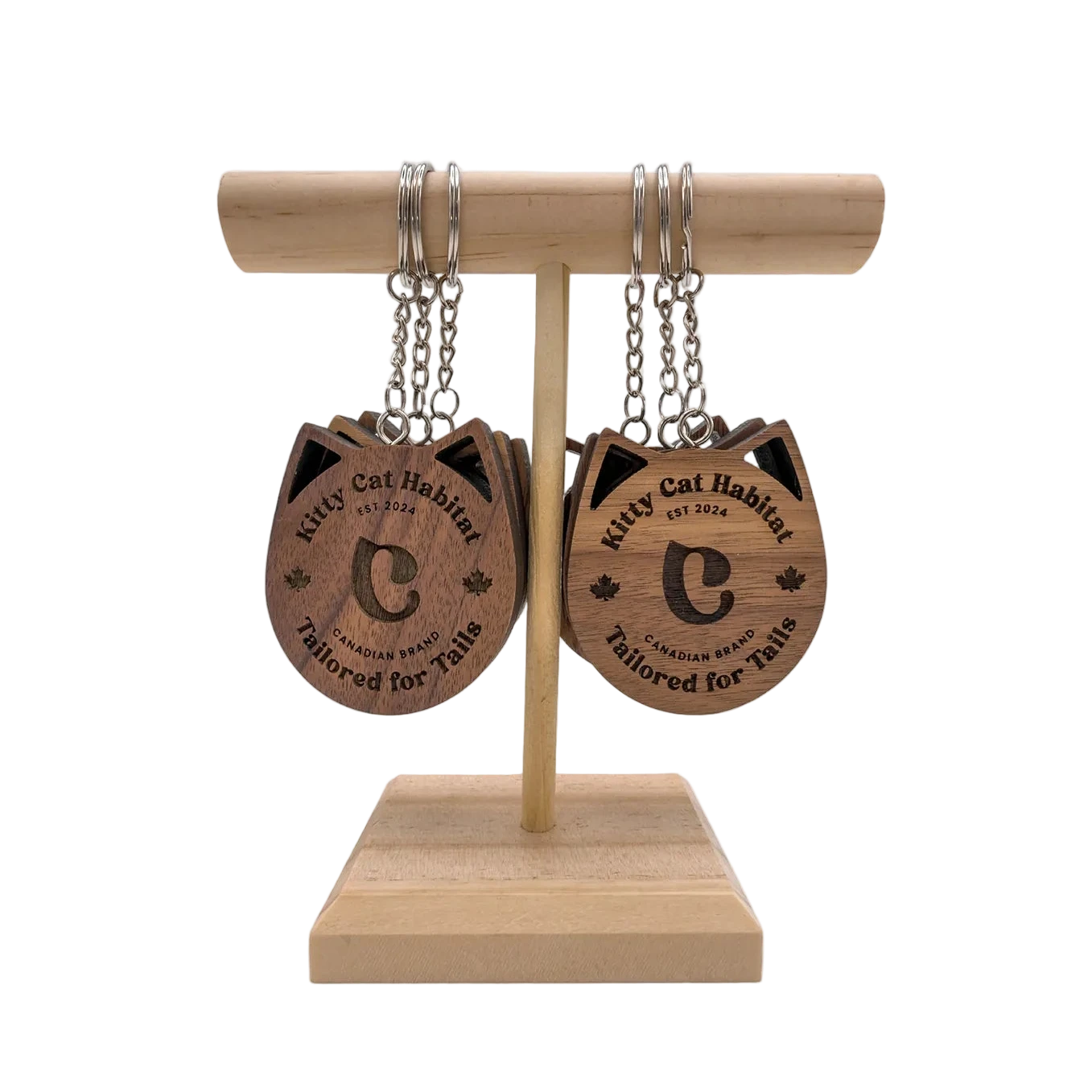 Several walnut wooden cat head keychains showing the logo side hanging on a wooden display stand on a light background.